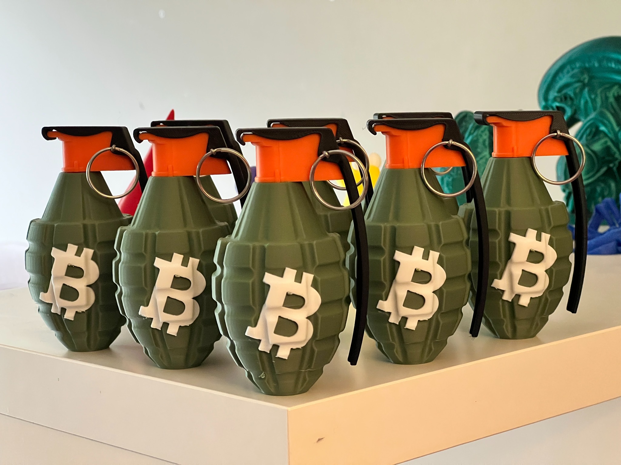 Several finished OPUSmakes Bitcoin grenade desk displays arranged together on a shelf
